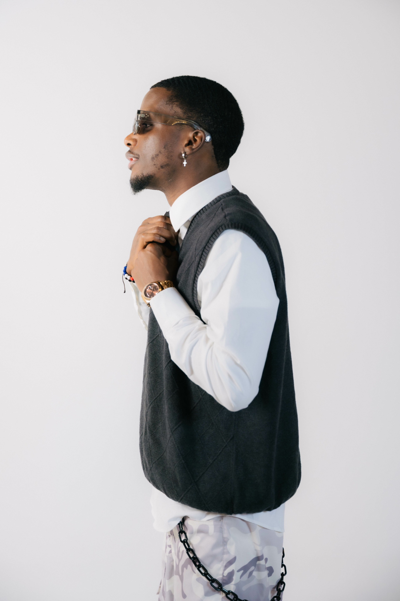 Side view of a person wearing sunglasses, a white shirt, and a dark vest, holding a strap over shoulder.