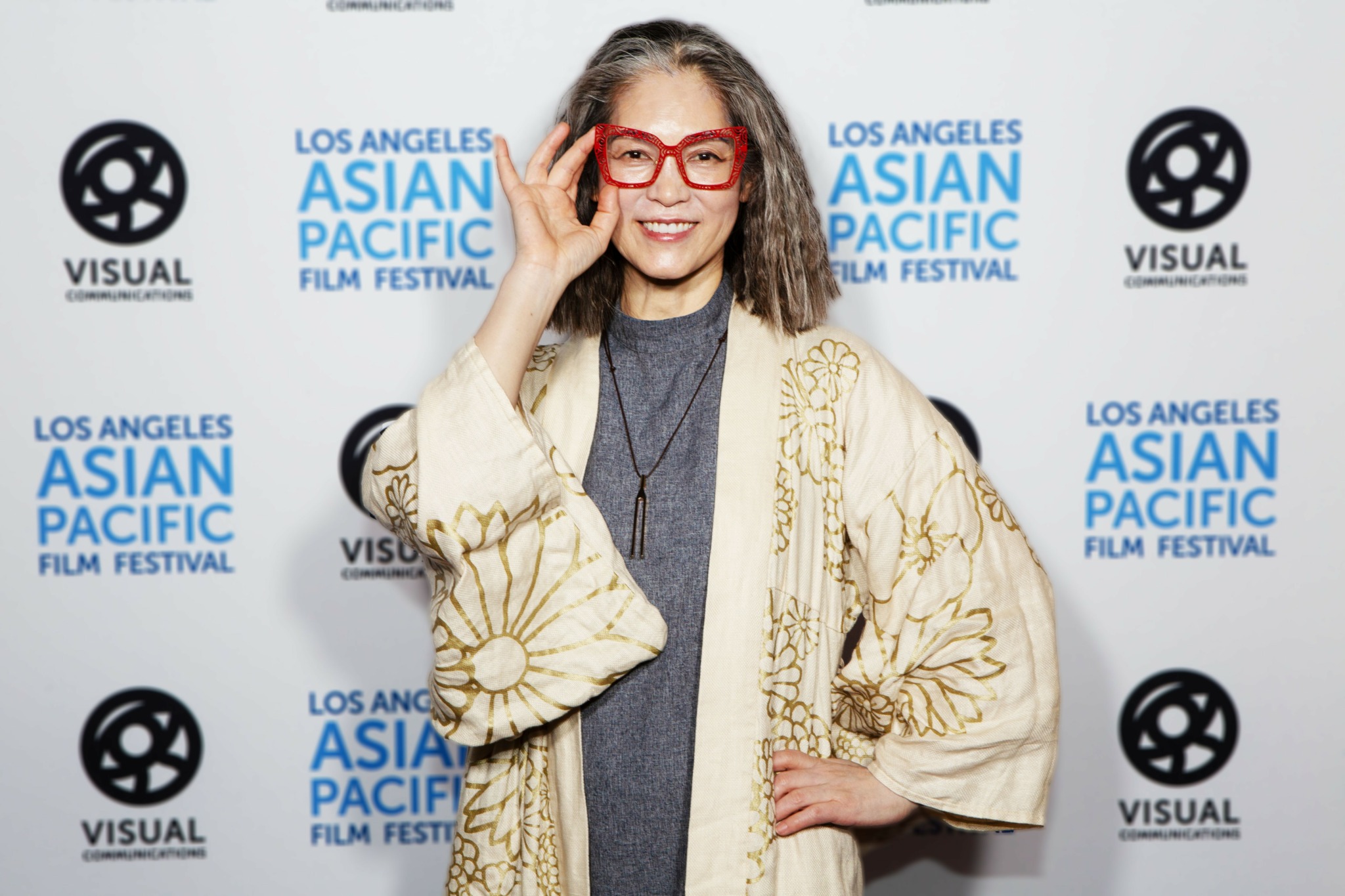 Woman with glasses and long hair smiling, standing in front of a backdrop with festival logos.