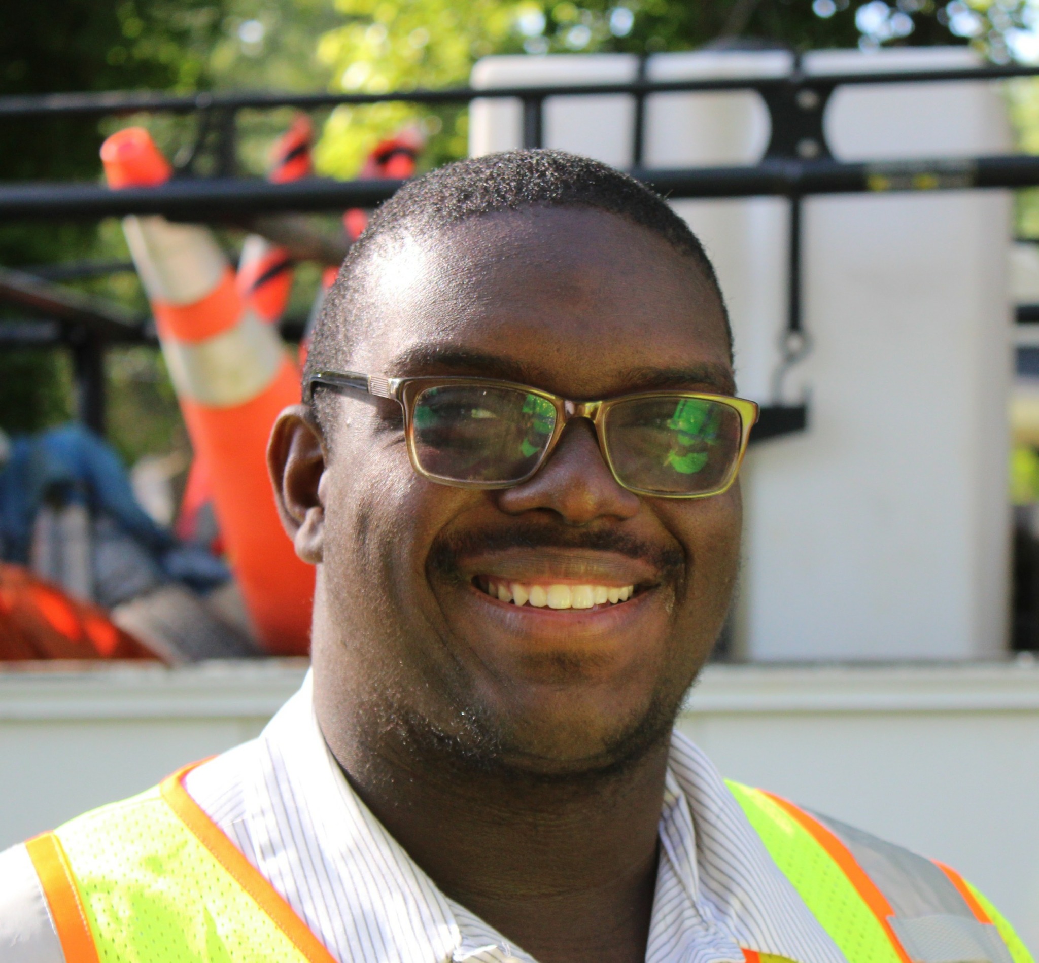 Smiling man wearing glasses and a high-visibility vest outdoors.