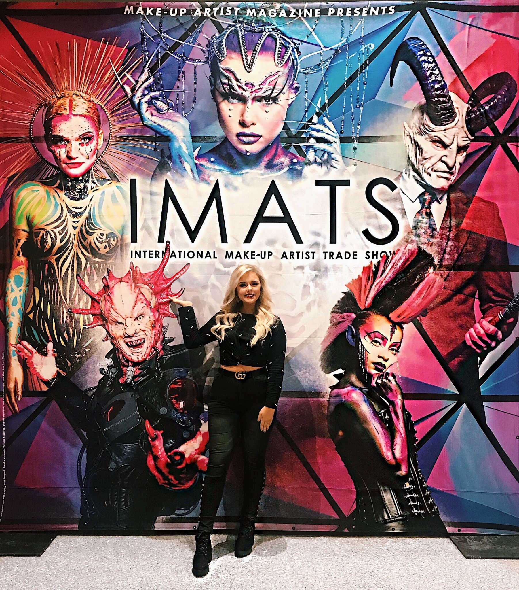 Person standing in front of a colorful, geometric backdrop with makeup-themed artwork and the word 'IMATS'.