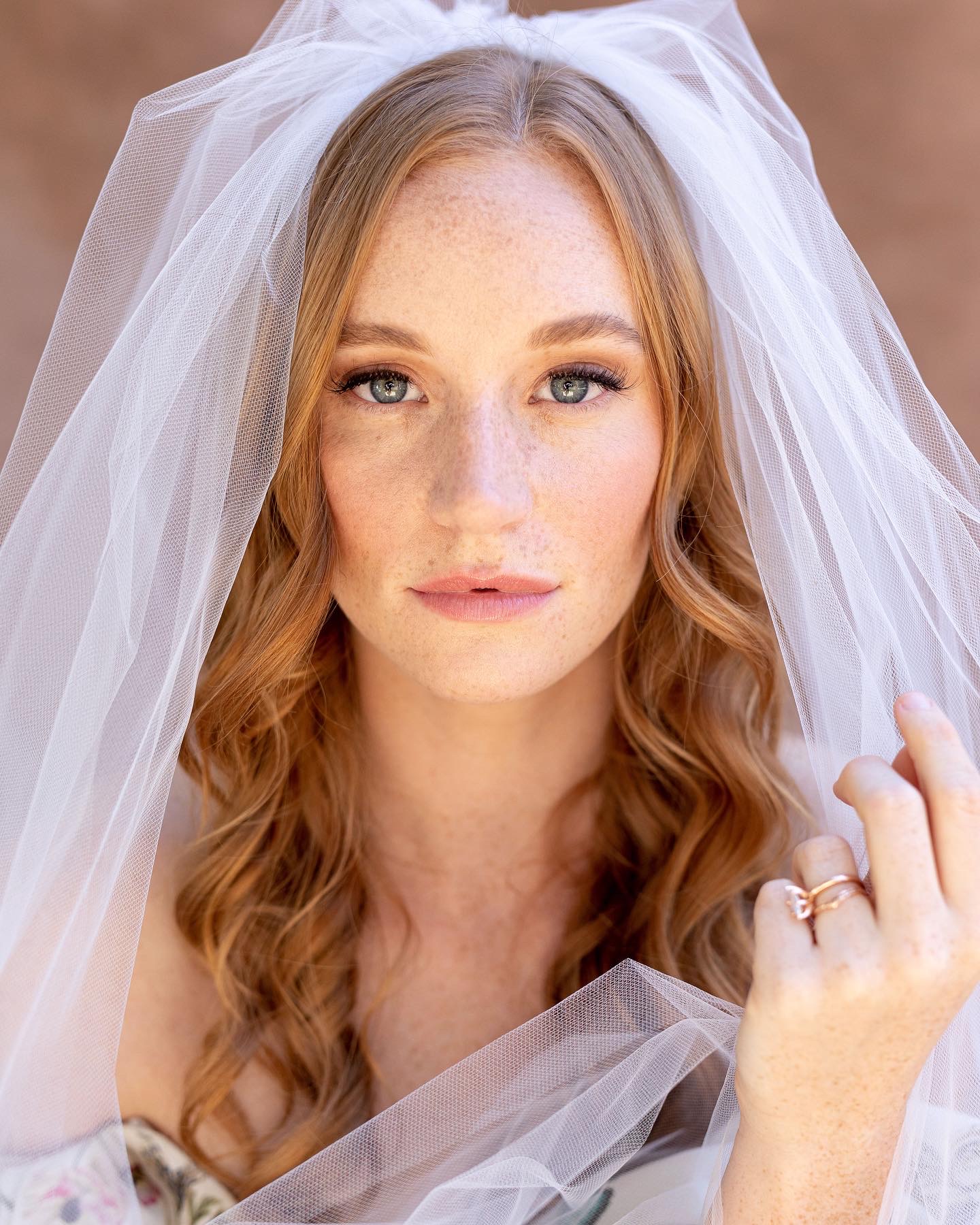 Woman with long wavy hair, wearing a wedding veil, looking directly at the camera.