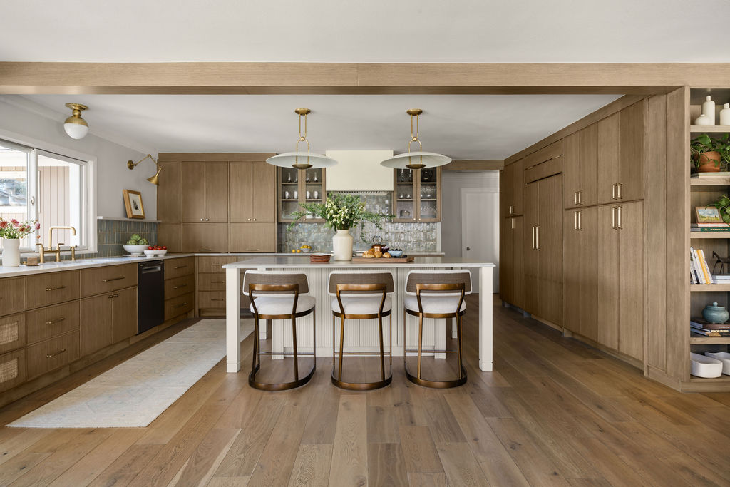 Modern kitchen with wooden cabinets, white island with four chairs, and open shelving with books and decor.