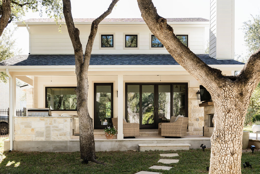 Front view of a house with large windows, a porch, and two trees in the yard.