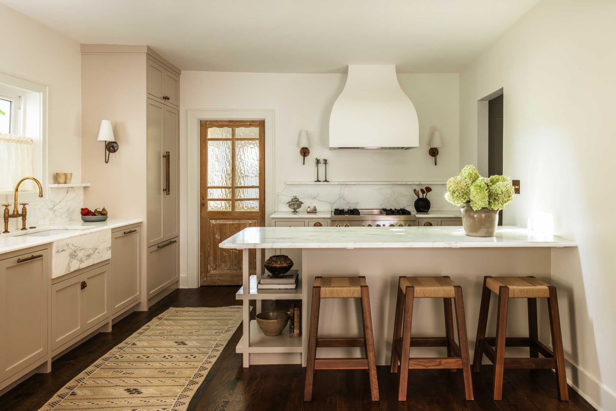 Kitchen with white cabinets, a stove, a countertop with flowers, and three wooden stools at the breakfast bar.