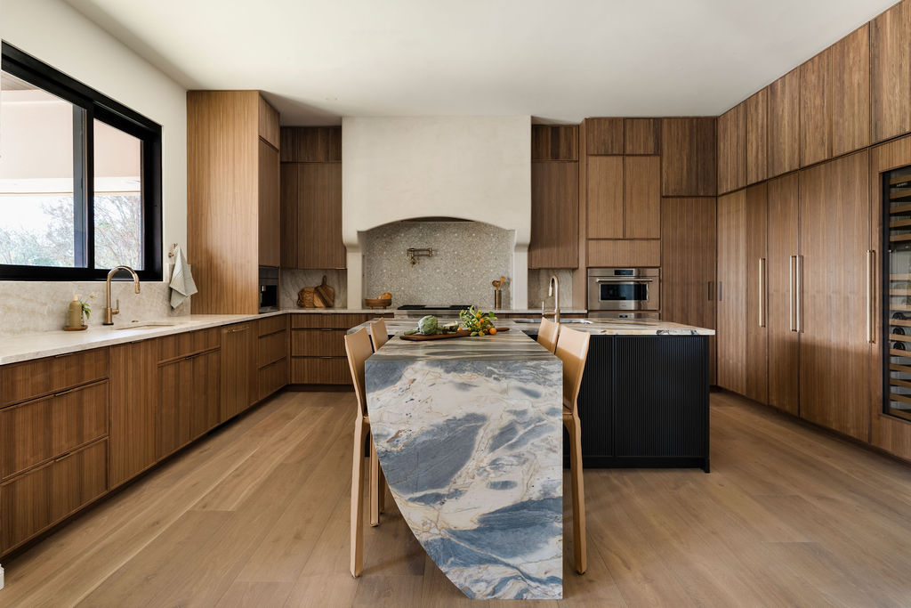 Modern kitchen with wooden cabinets, a marble island, and a window with a view outside.