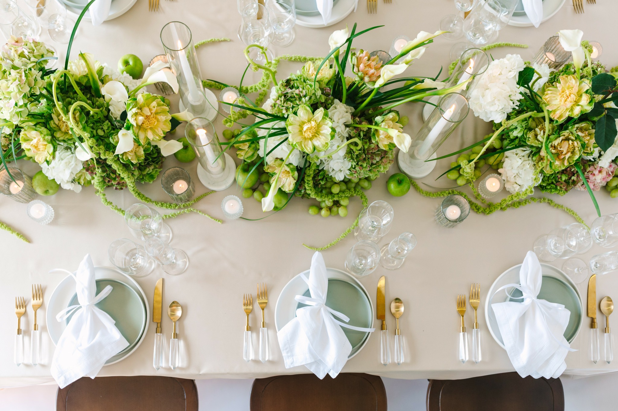 Table with floral centerpieces, white tablecloth, and place settings with napkins and glassware.