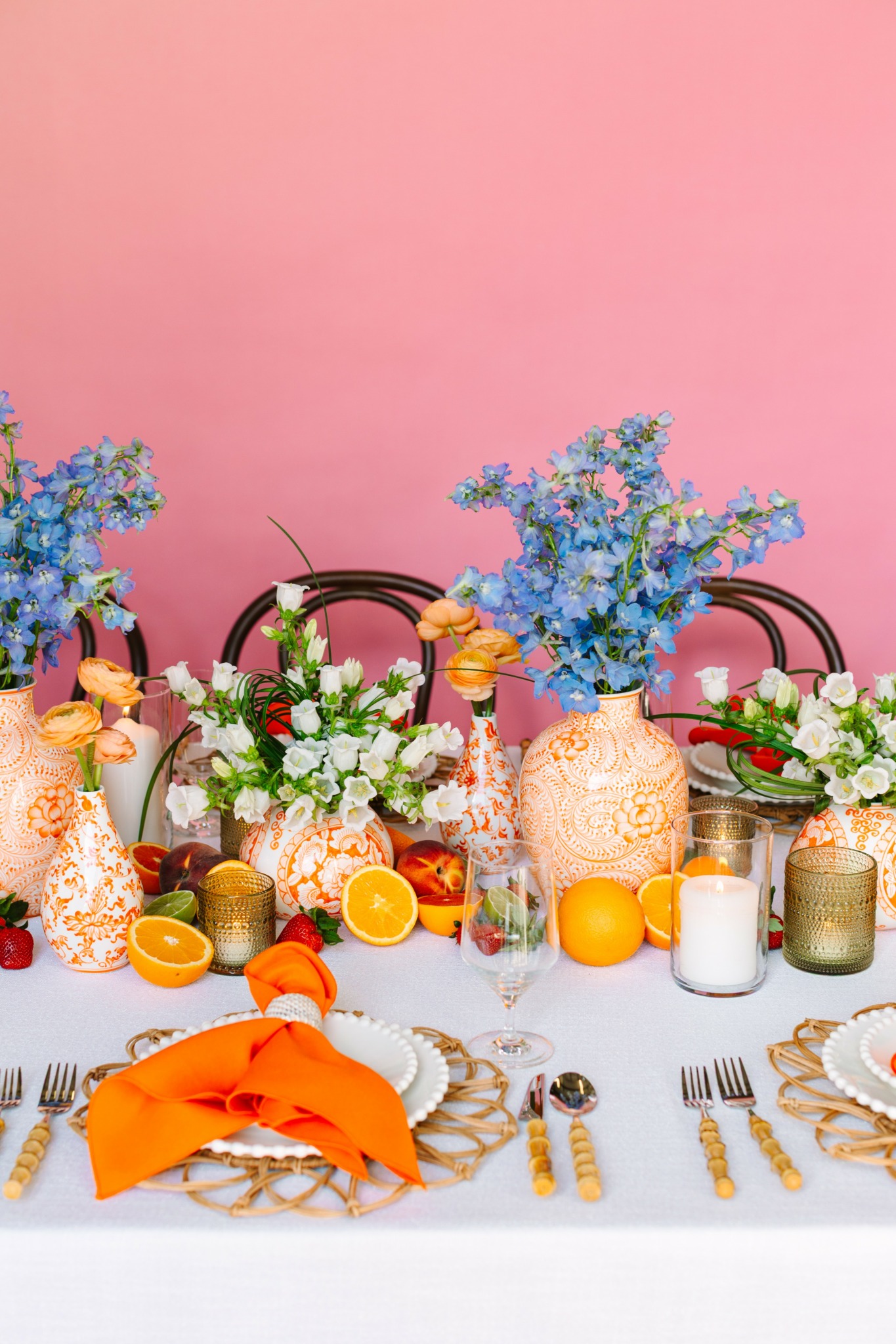 Table decorated with blue and pink flowers, oranges, candles, and orange napkins on a white tablecloth.