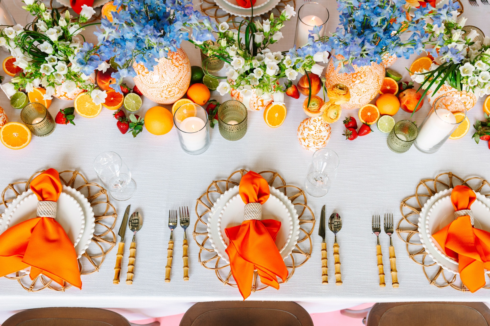 Table setting with floral centerpiece, orange napkins, plates, glasses, and cutlery on a white tablecloth.
