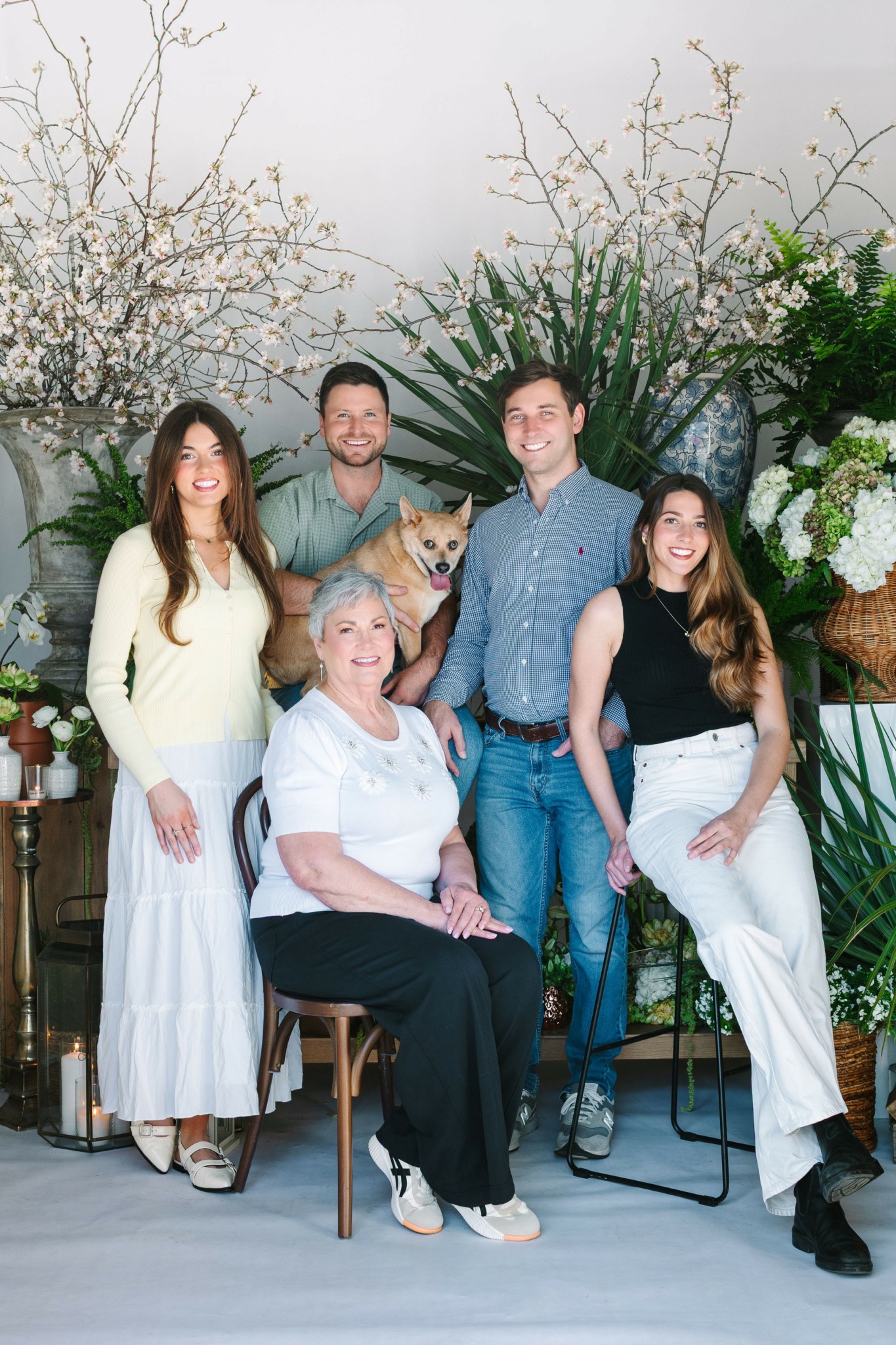 Group of five people, three women and two men, posing indoors with plants and flowers in background.