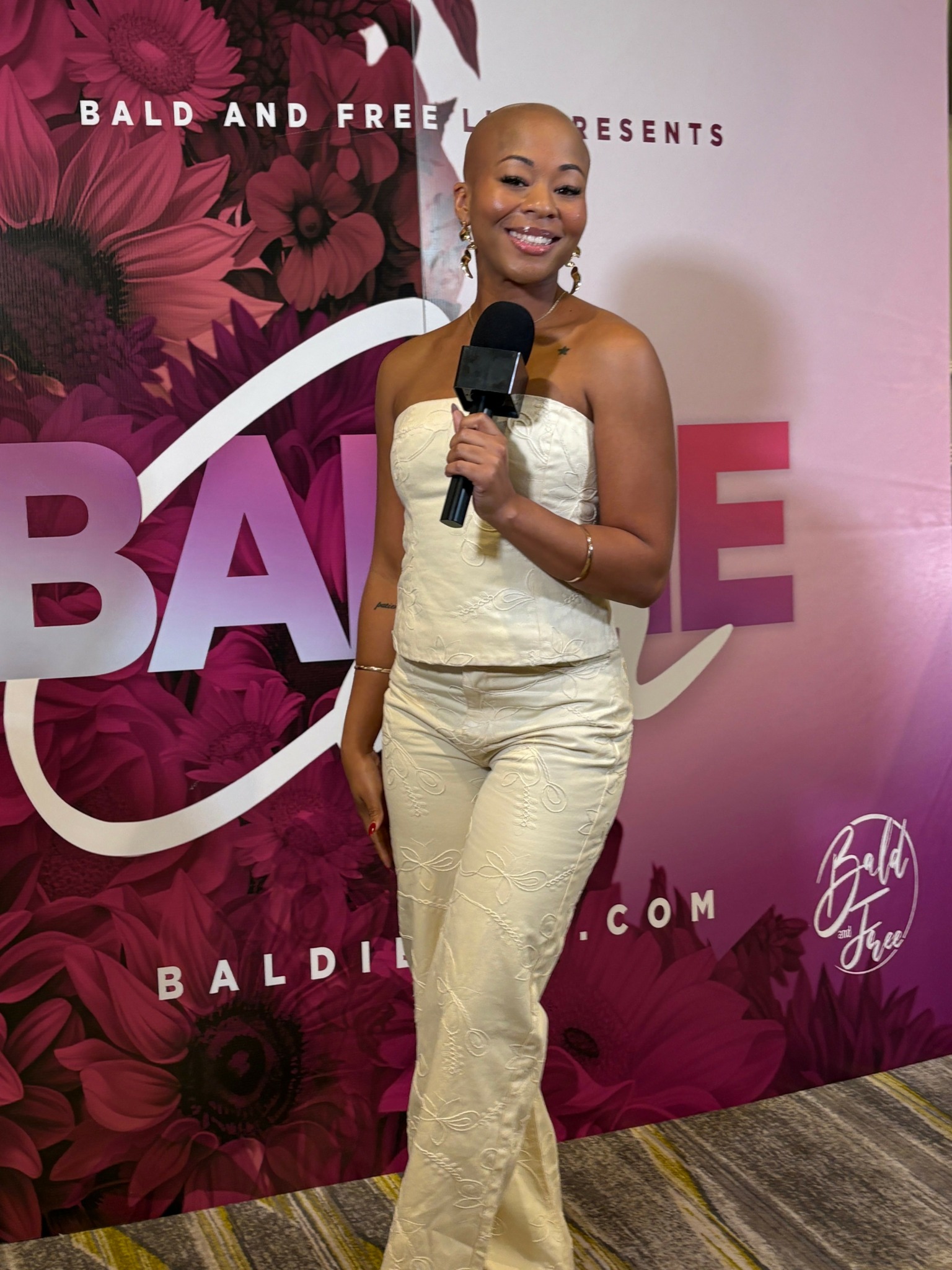 Smiling woman holding microphone in front of pink and purple floral backdrop with text.