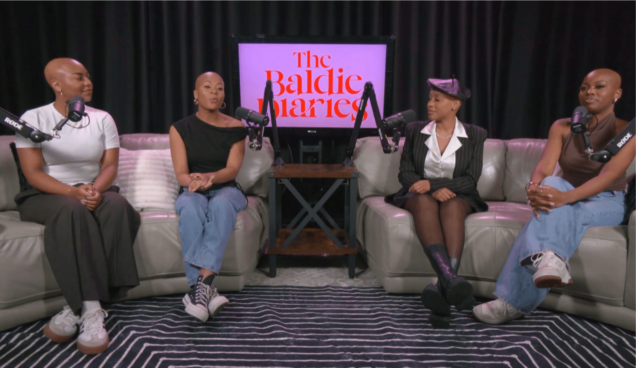 Four women sit on a sofa in a studio with a black curtain background and a screen displaying 'The Ballice Marcie'.