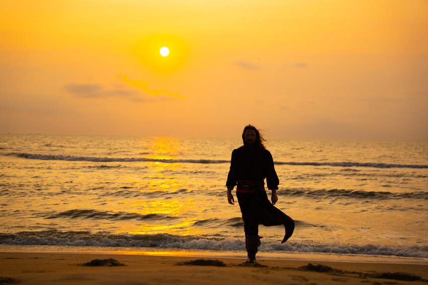 Person standing on beach at sunset with ocean waves in background.