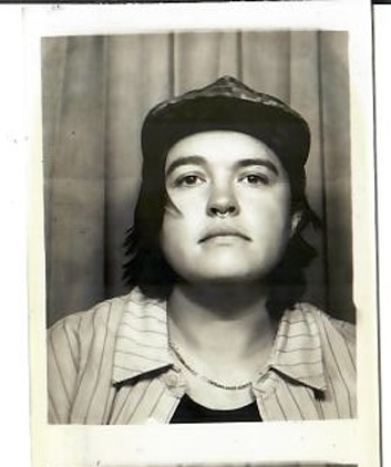 Black and white portrait of a person wearing a cap and striped shirt, looking directly at the camera.