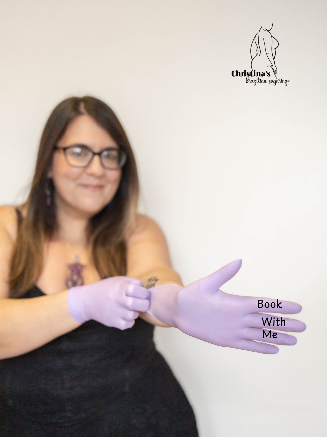 Woman wearing glasses and purple gloves, holding a sign that reads 'Book With Me'.