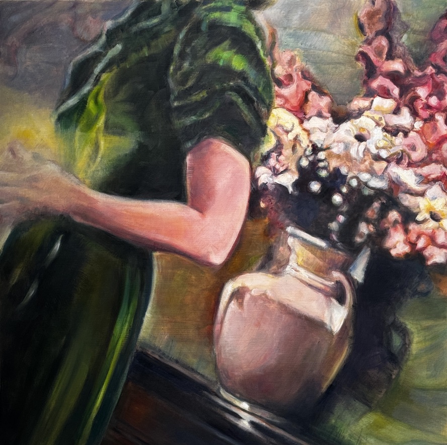 Person in green dress standing next to a vase of pink and white flowers on a table.