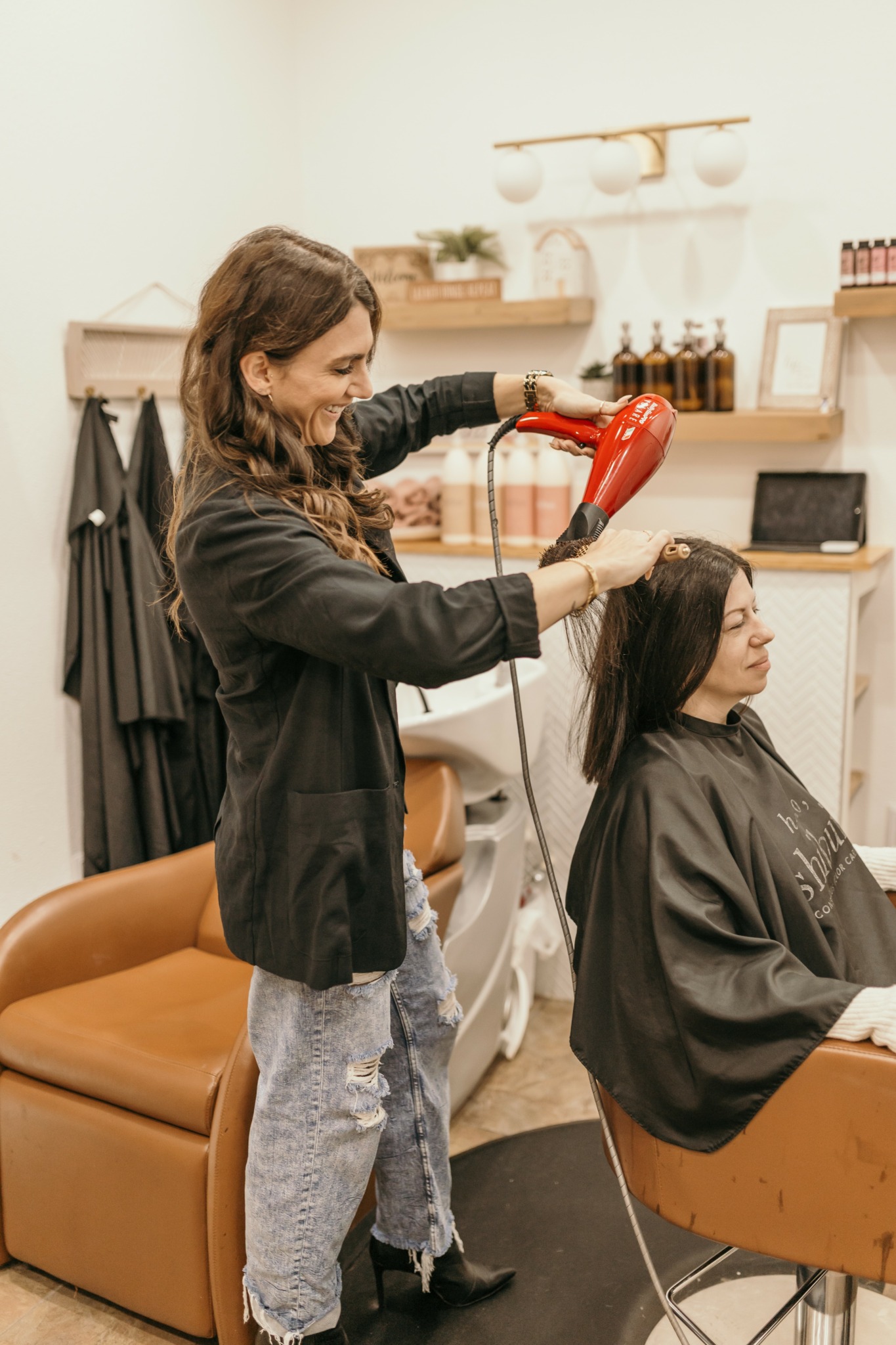 Hairdresser drying a client's hair with a red hairdryer in a salon.