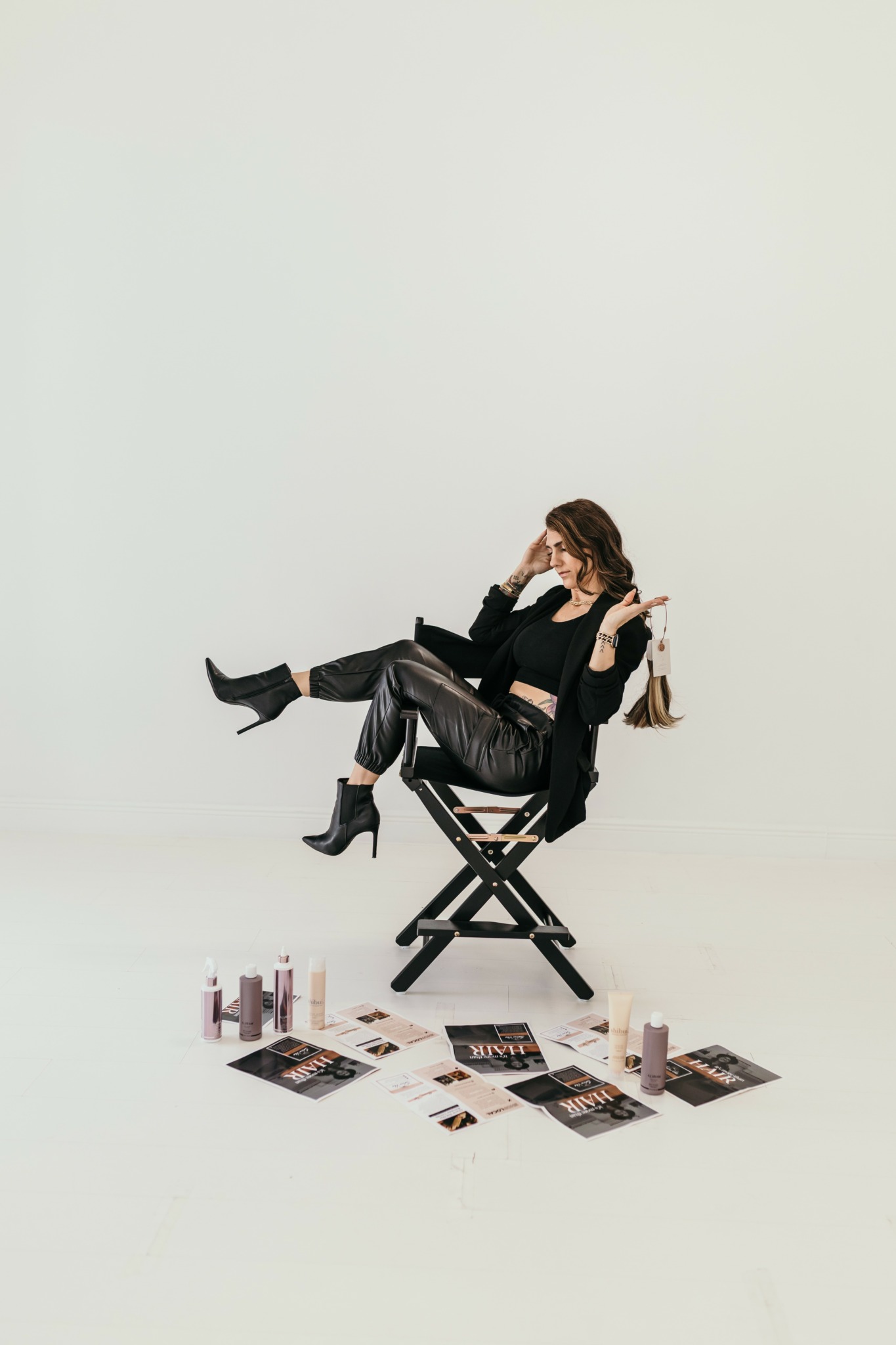Woman sitting on a director's chair with makeup products and magazines on the floor around her.