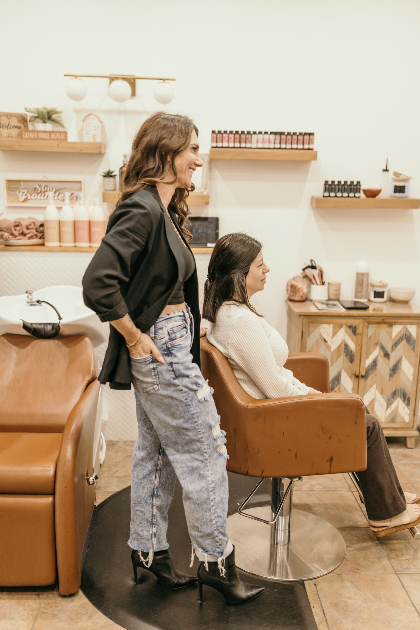 Woman standing next to seated girl in a salon with shelves of nail polish and beauty products.