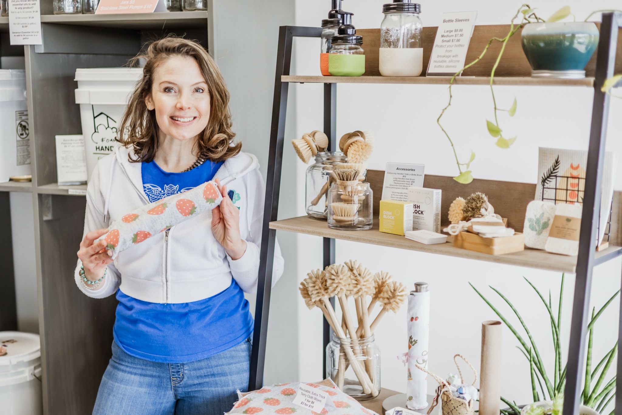 Woman with curly hair smiling and holding a pink object in a store with shelves of products.