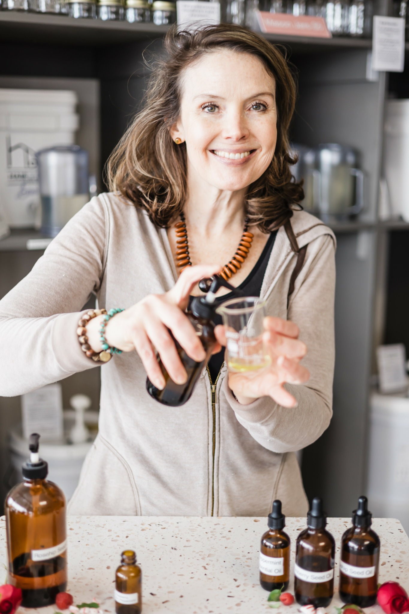Woman pouring liquid from a bottle into a glass in a laboratory or pharmacy setting.