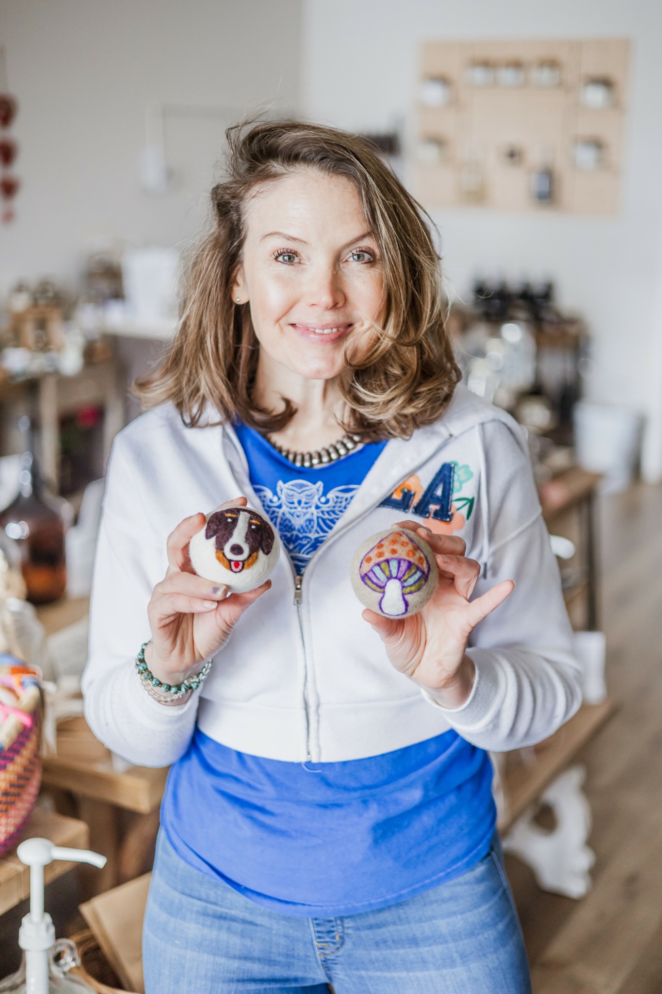 Woman with shoulder-length hair holding decorated cupcakes in a cozy kitchen.