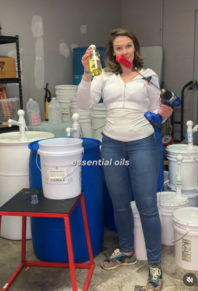 Woman holding a yellow bottle and a blue container, standing in a room with shelves and containers.