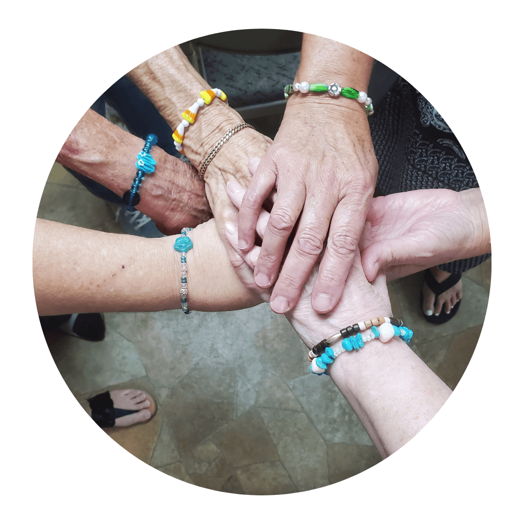 Multiple hands stacked together, each wearing colorful beaded bracelets, symbolizing unity and friendship.