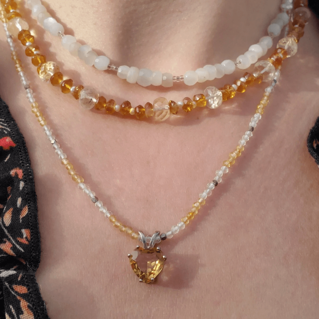 Three layered necklaces with beads and a heart-shaped pendant on a person's neck.