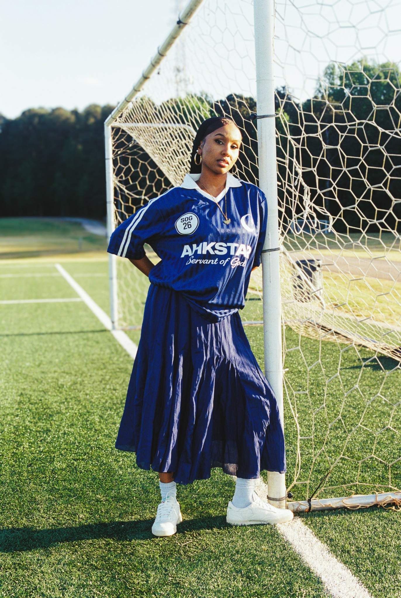 Young woman in blue sports uniform standing next to a soccer goal on a field.