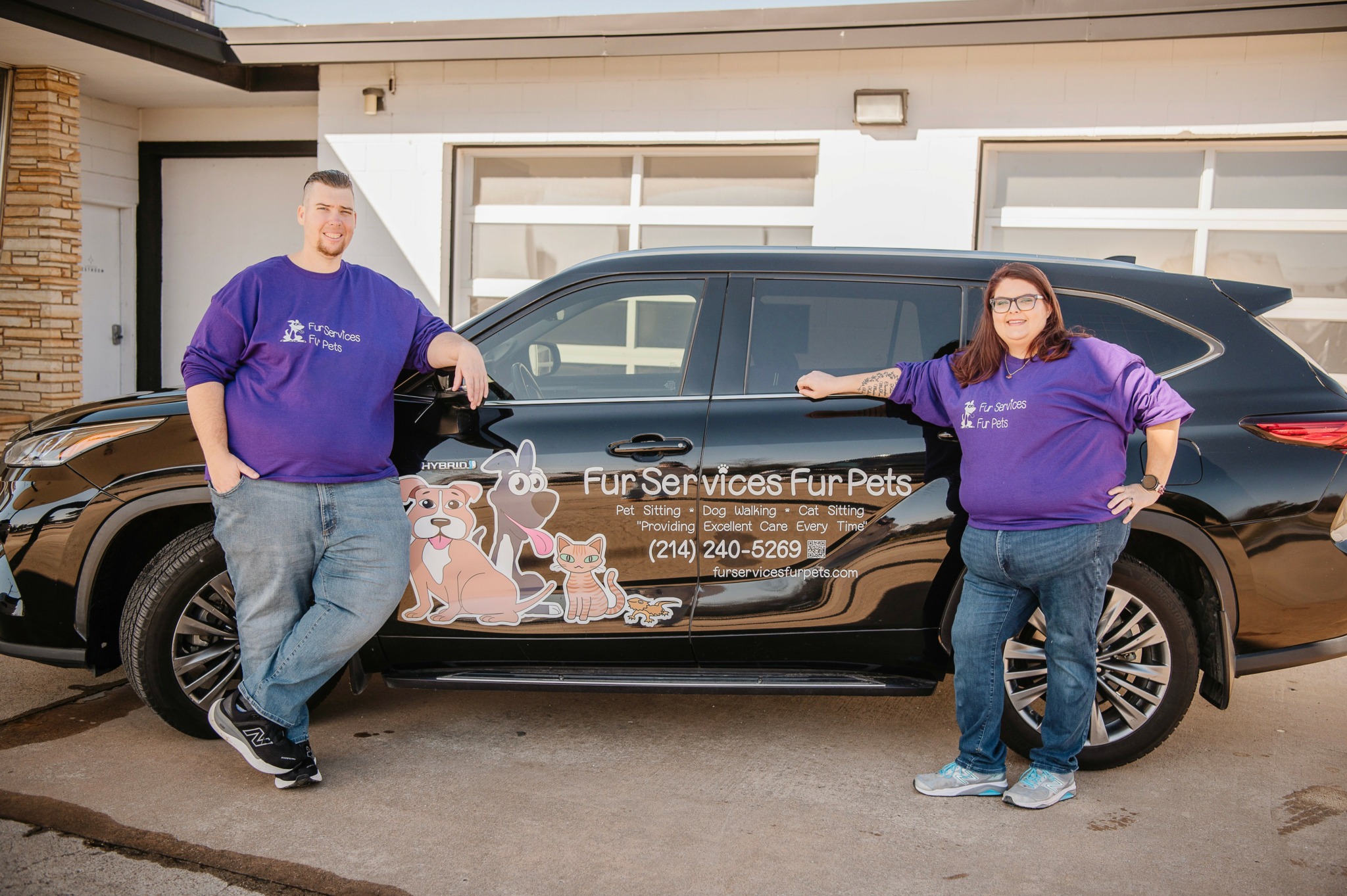 Two people stand beside a black car with a colorful pet-themed wrap, in front of a garage.