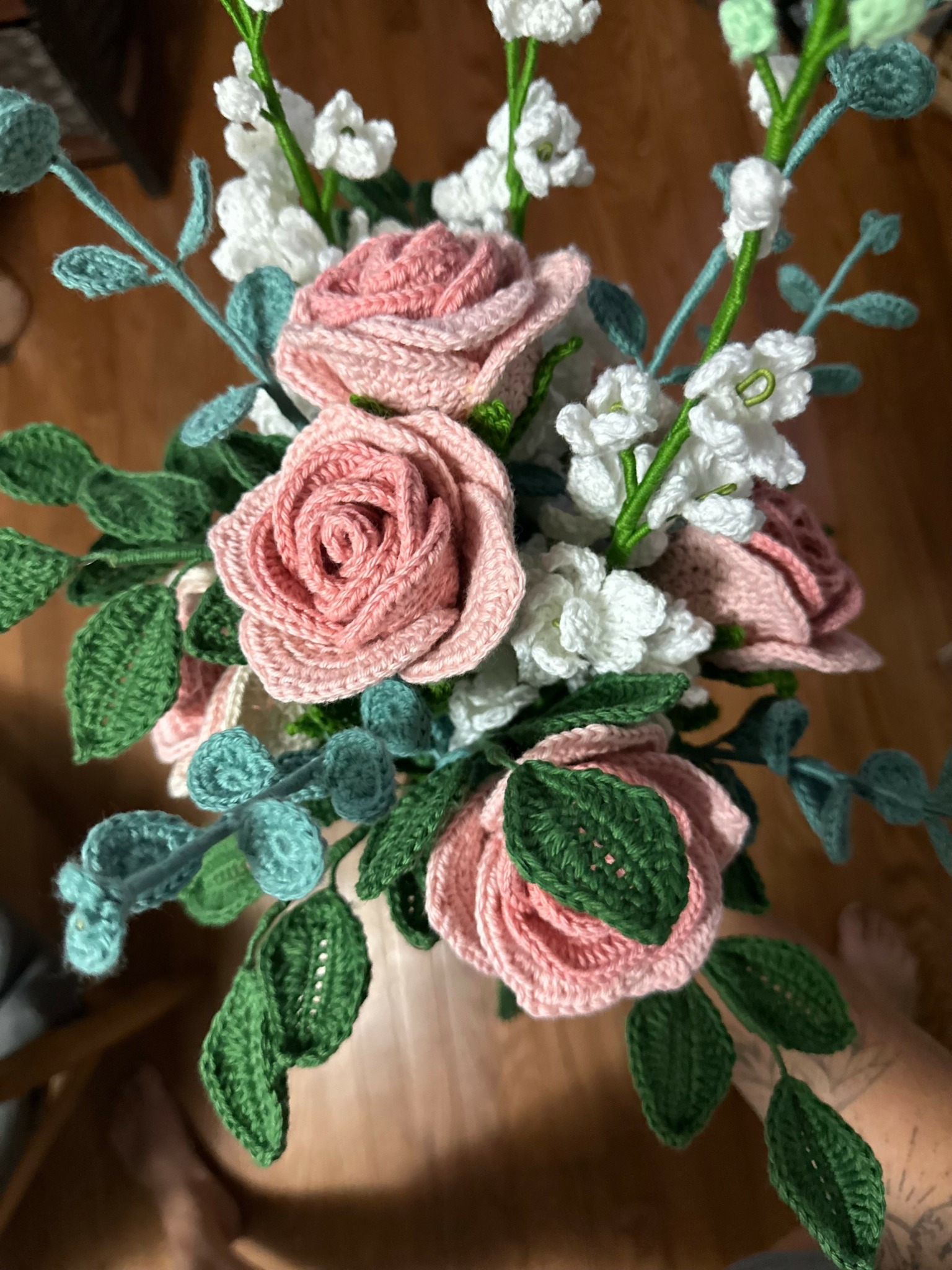Artificial pink roses, white small flowers, and green leaves arranged in a bouquet.