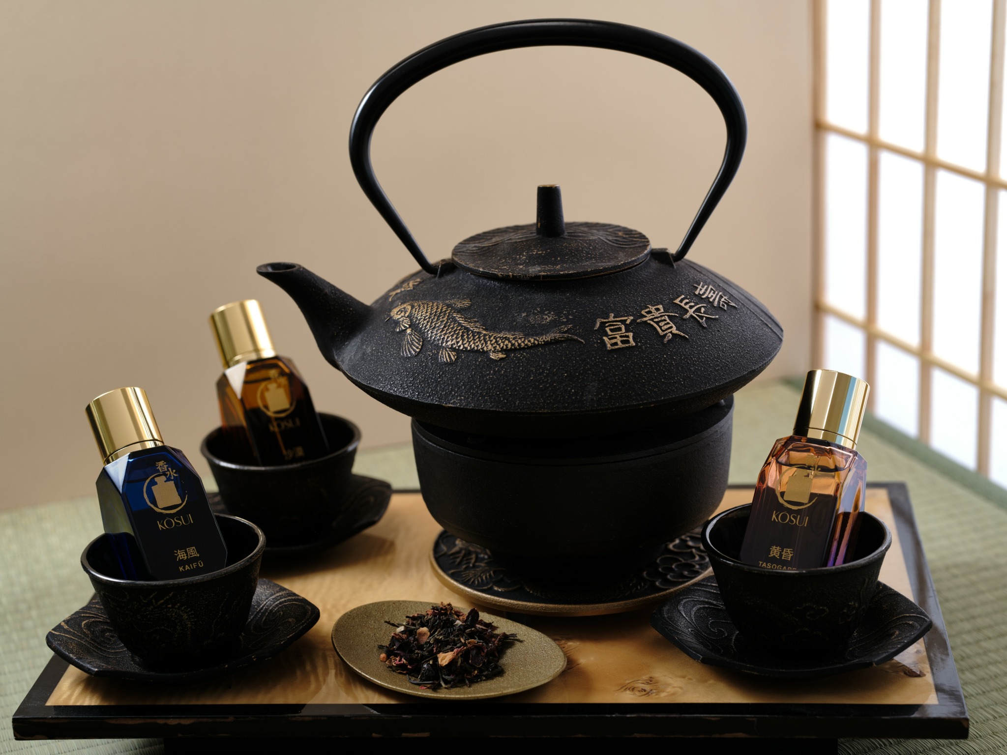 Black teapot with gold Chinese characters, surrounded by four small bottles in black cups, on a tray with a small dish of tea leaves.