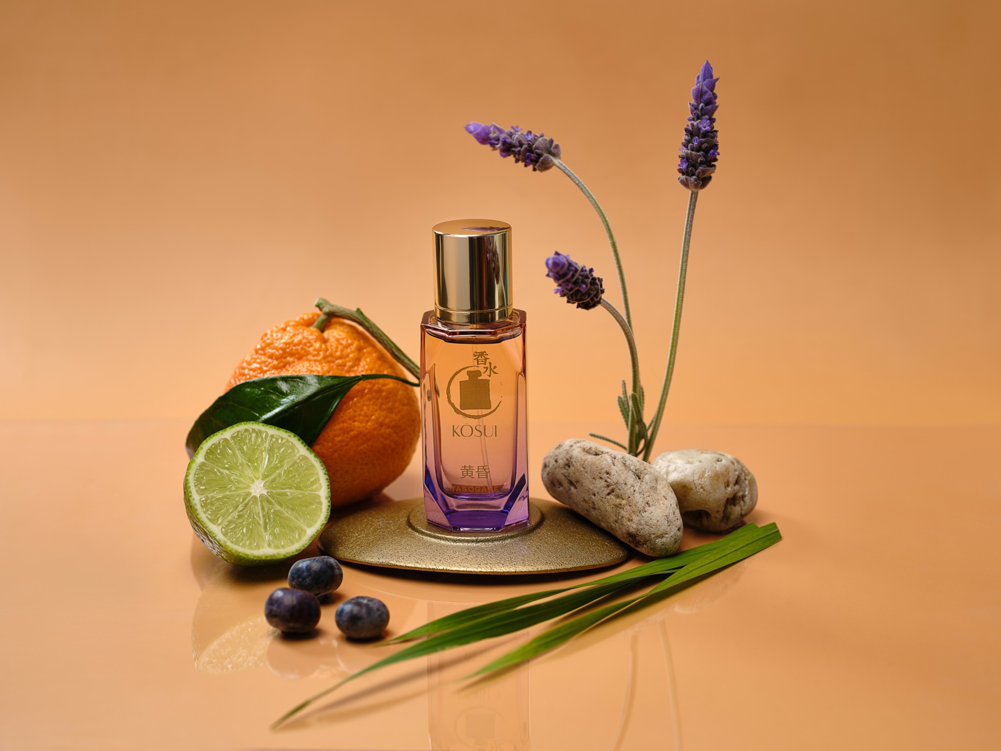 A purple perfume bottle surrounded by orange, lime, blueberries, lavender flowers, and rocks on a beige background.