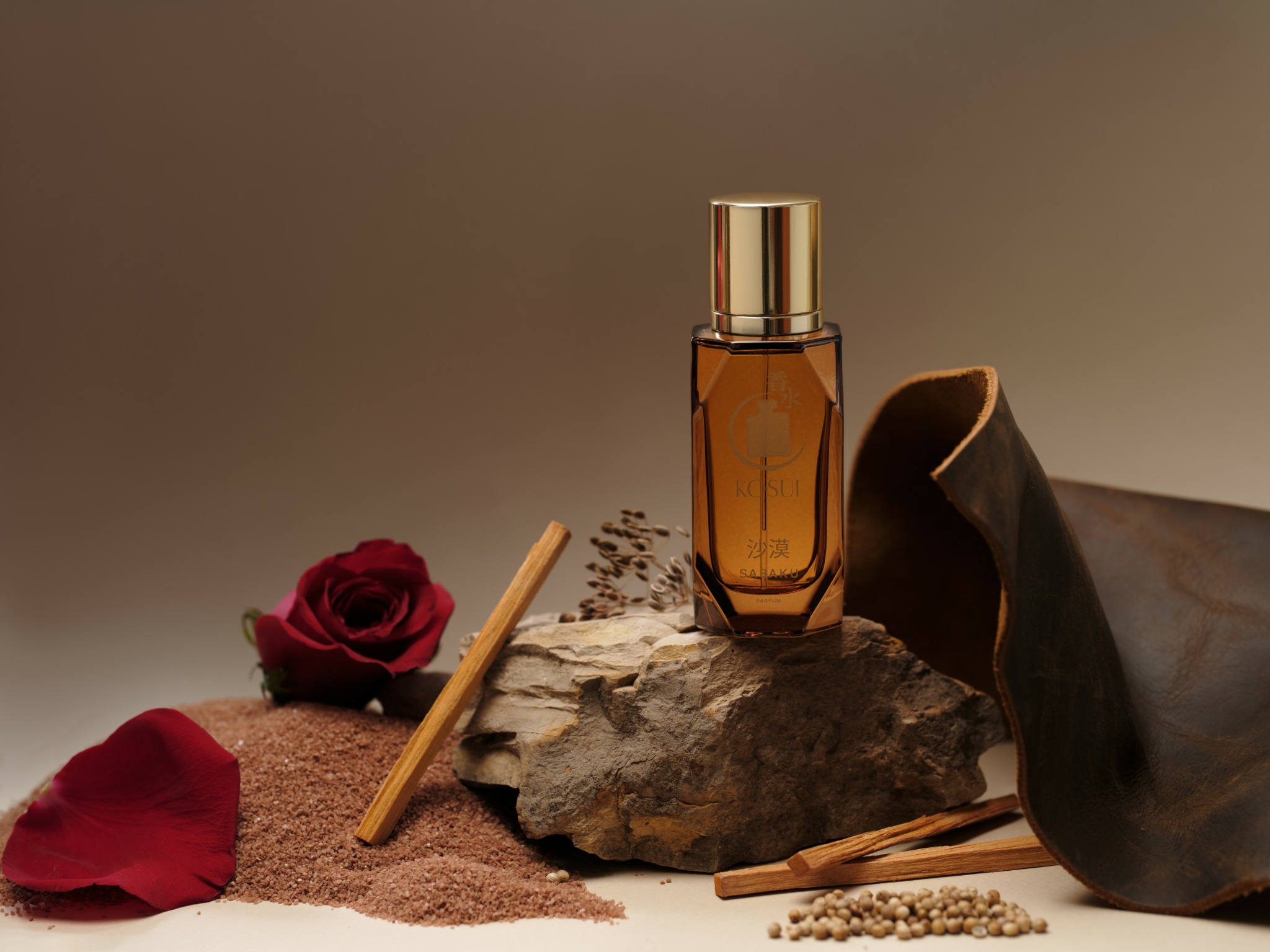 Amber bottle on rock with rose petals, cloth, and cinnamon sticks in background.
