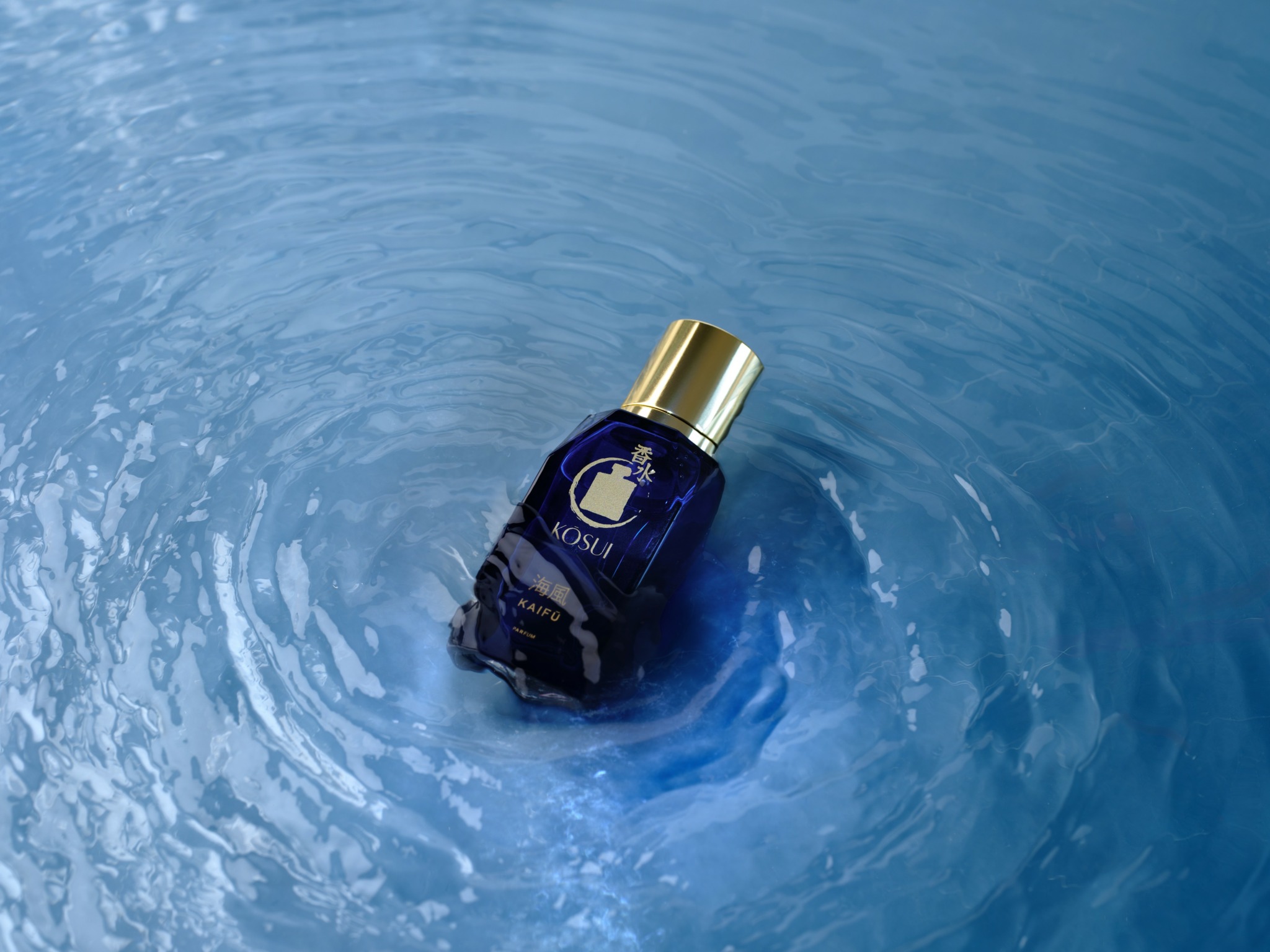 Blue bottle with gold cap floating in water with ripples around it.