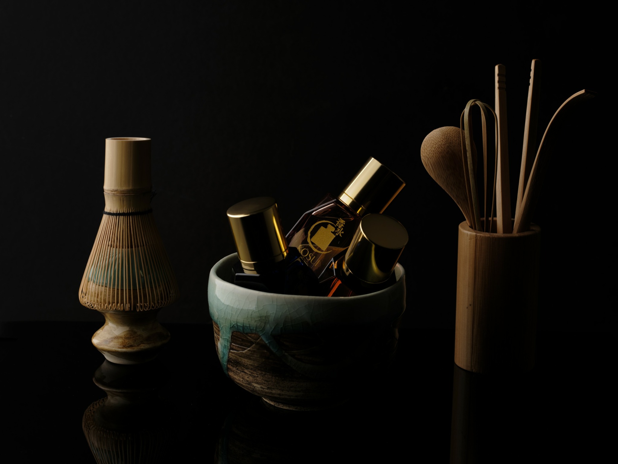 Vase, bowl with bottles, and container with sticks against a black background.