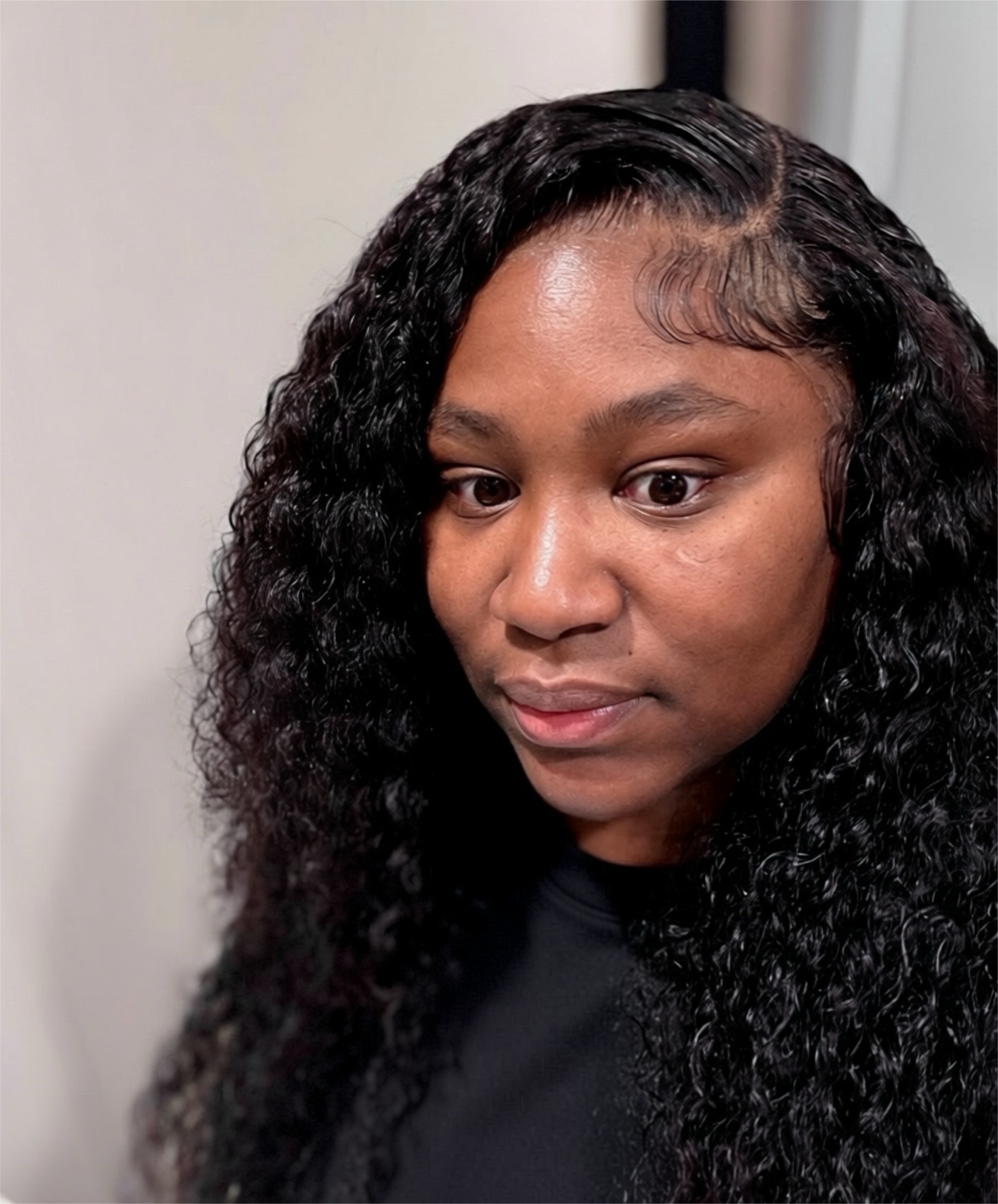 Woman with long, curly black hair looking down, indoors with a neutral background.
