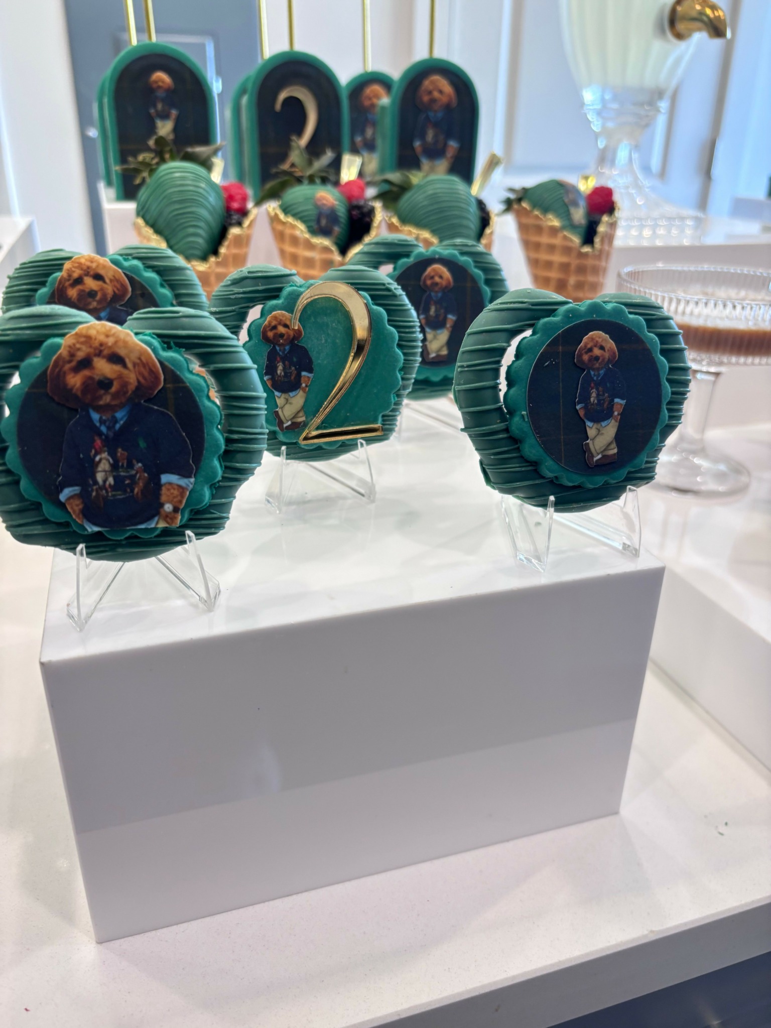 Display of decorated cupcakes with blue wrappers and images, on a white surface with a white box nearby.