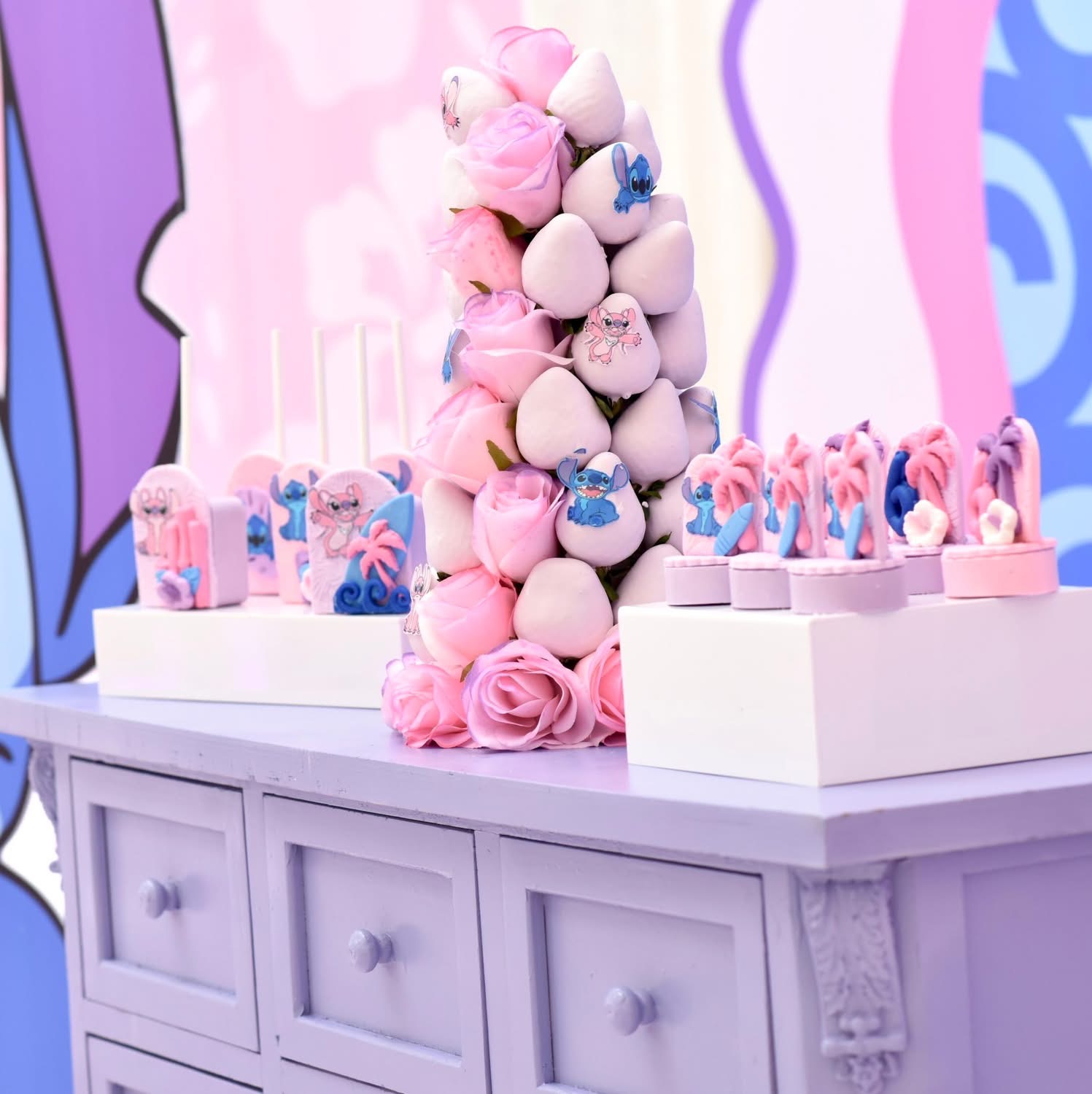 Decorative pink and white desserts and a tall cone of pink and white sweets on a white table.