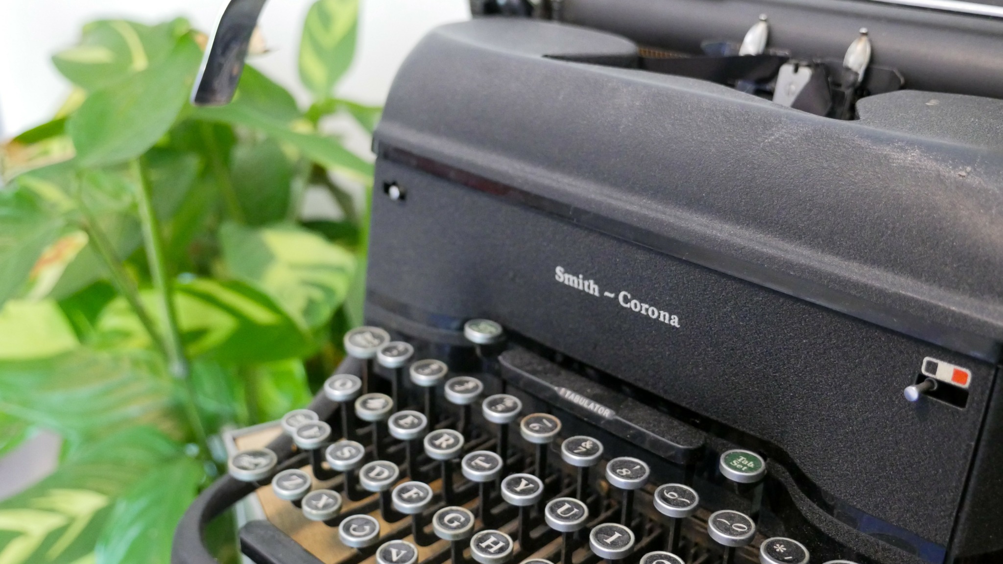 Close-up of a vintage Smith-Corona typewriter with round keys and a plant in the background.