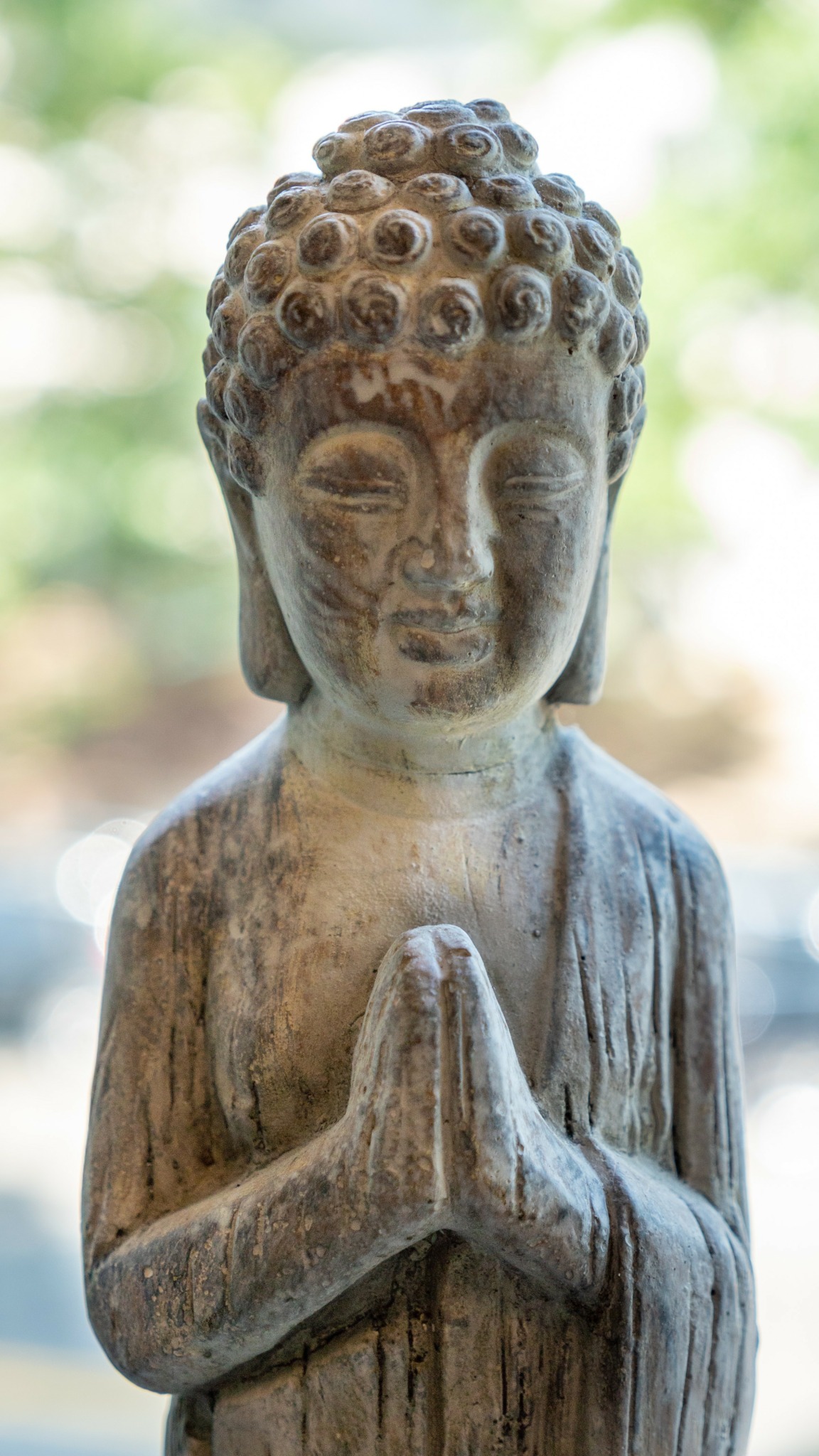 Wooden statue of a person with hands pressed together in prayer, curly hair, and closed eyes.
