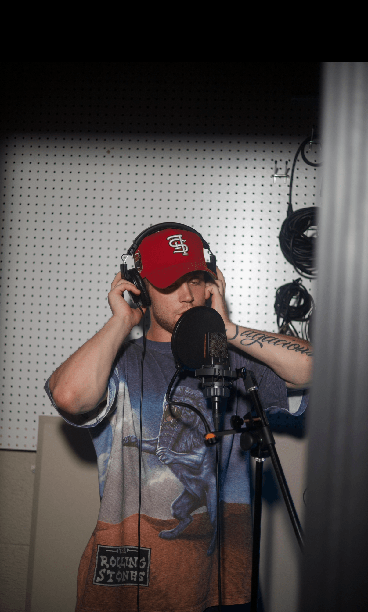 Person wearing a red cap and headphones in a recording studio, speaking into a microphone.