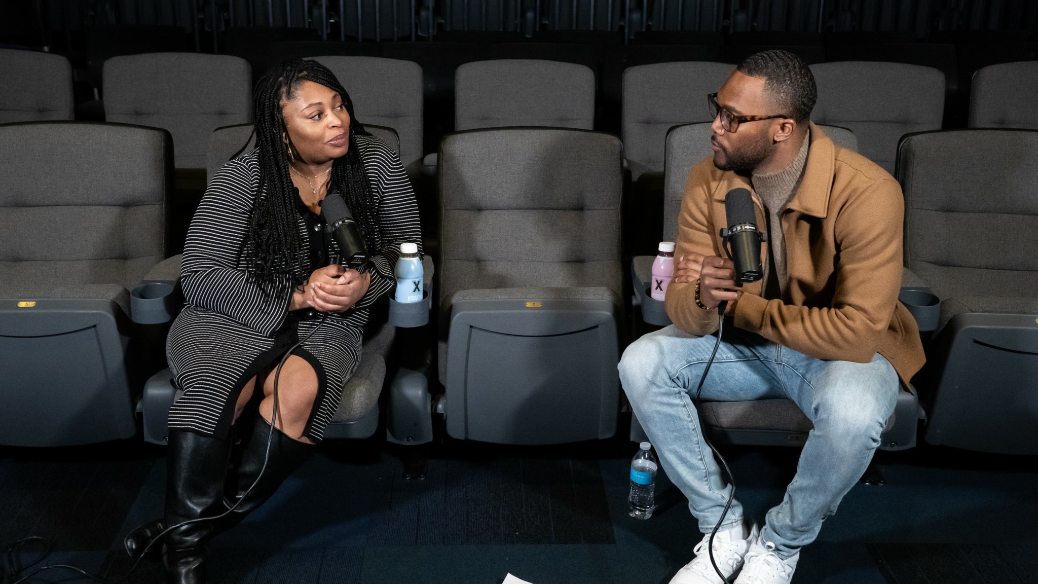 Two people sitting in a theater, engaged in conversation, with empty seats behind them.