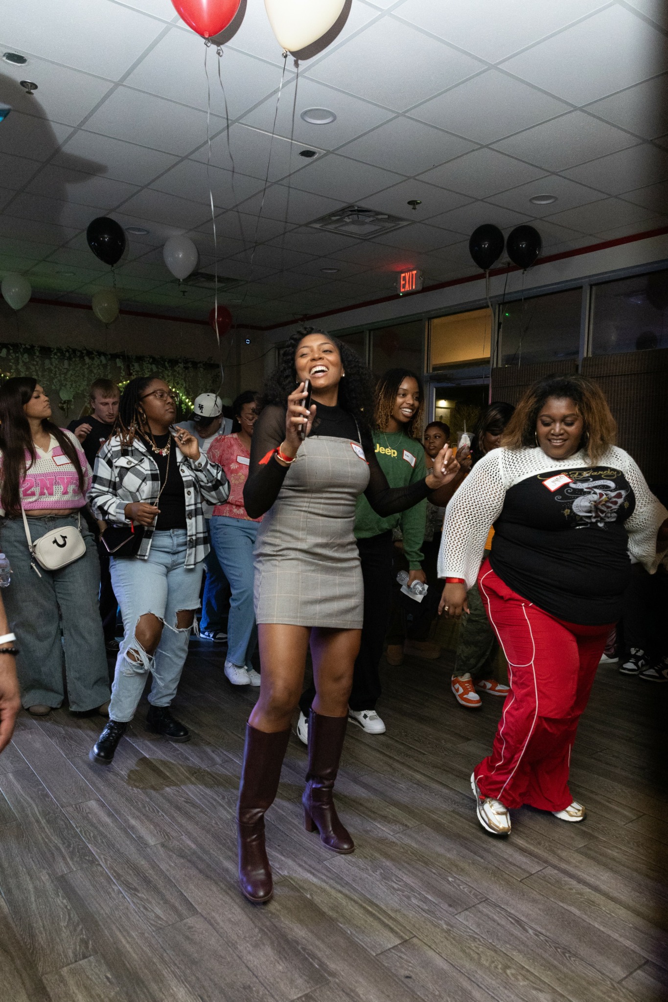 Group of women dancing indoors with balloons and decorations on ceiling, smiling and enjoying music.