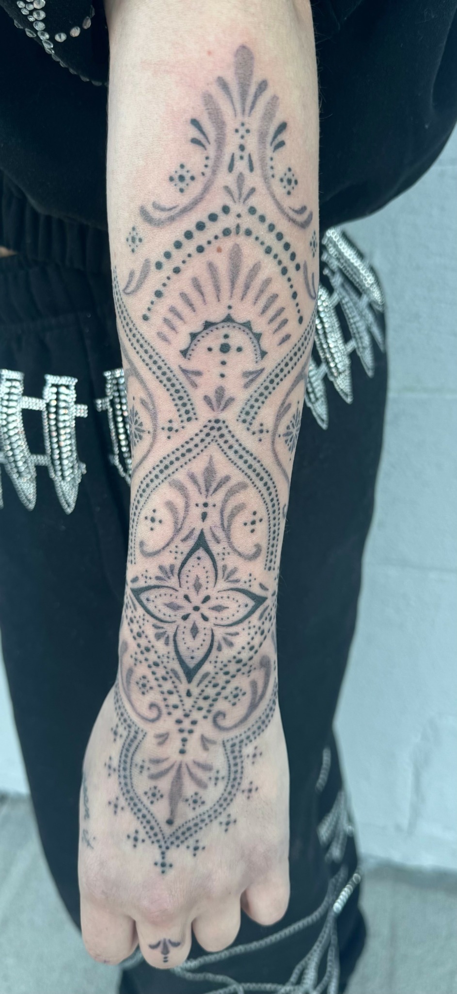 Forearm tattoo with symmetrical geometric and floral patterns in black ink.