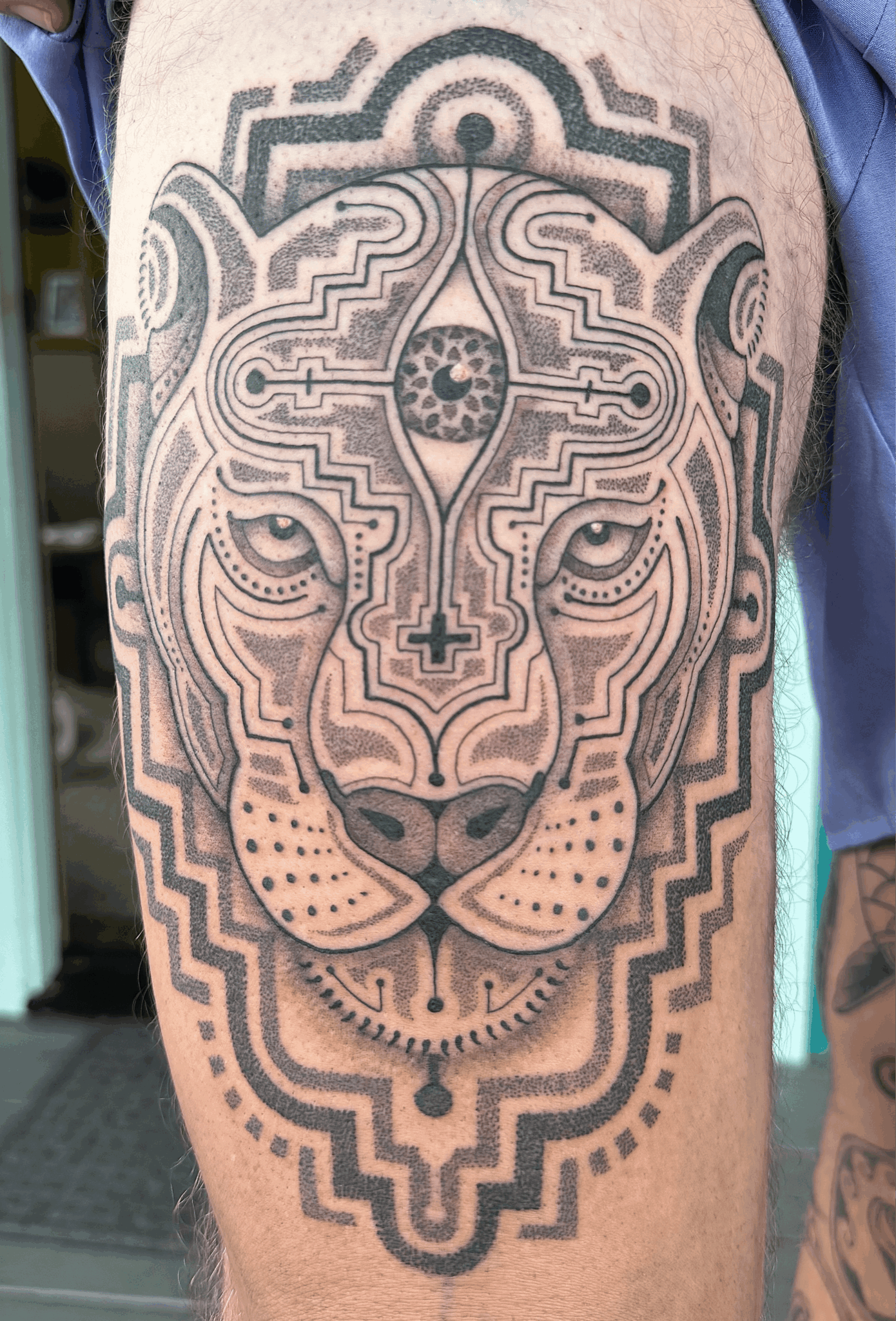 Lion face tattoo with geometric patterns and symmetrical design on person's arm.
