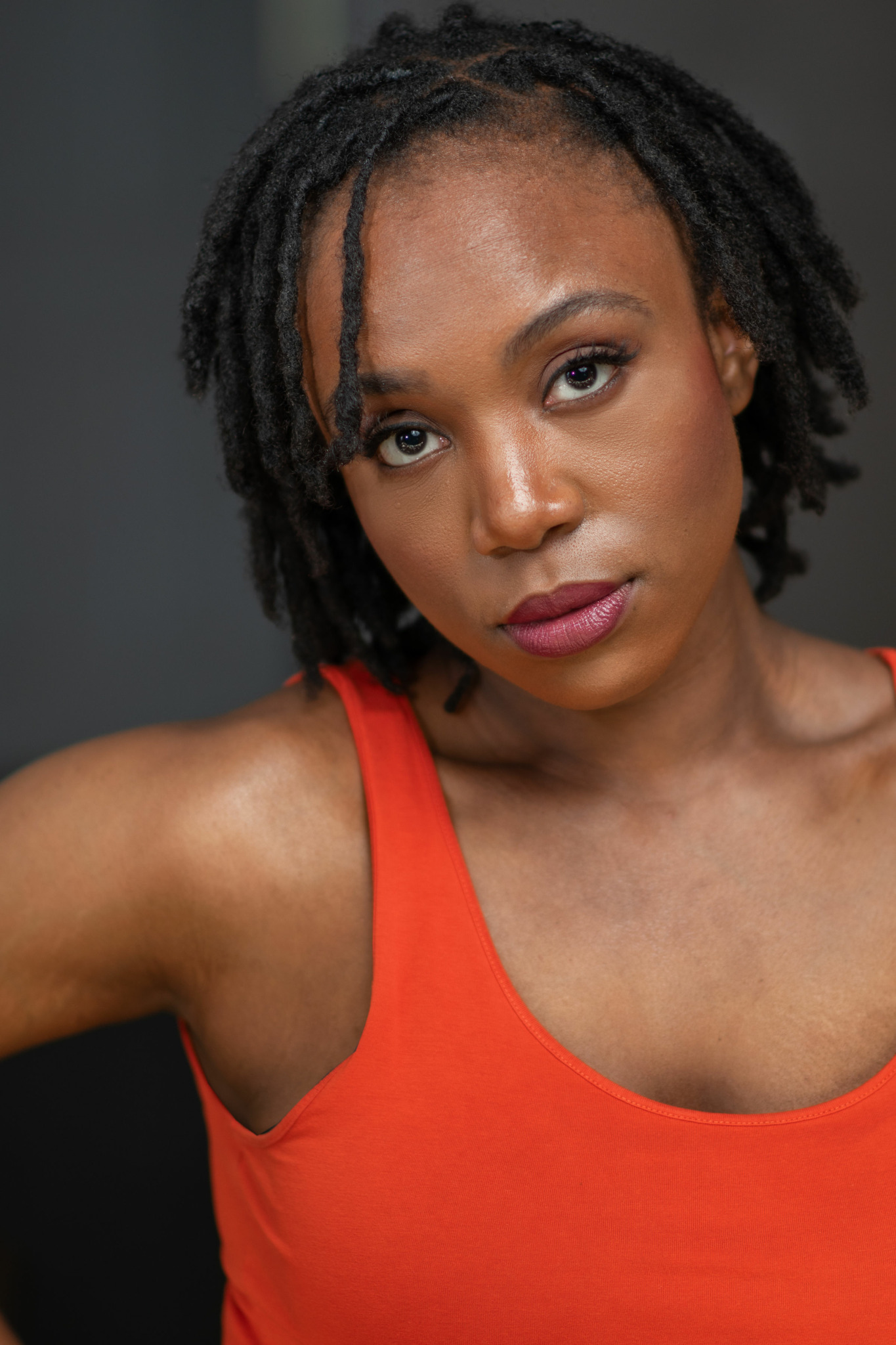 Close-up of a woman with natural hair wearing a red sleeveless top, looking at the camera.