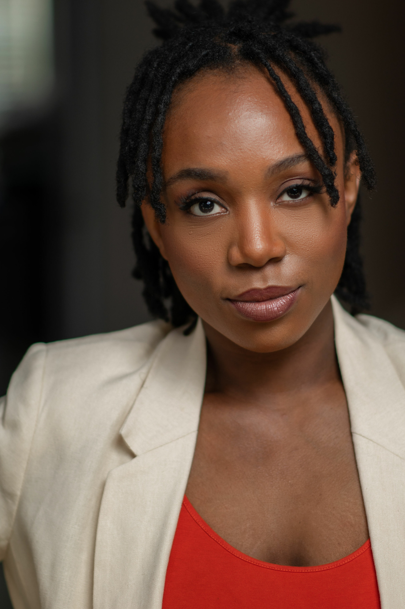 Close-up portrait of a woman with dreadlocks wearing a beige blazer and red top.