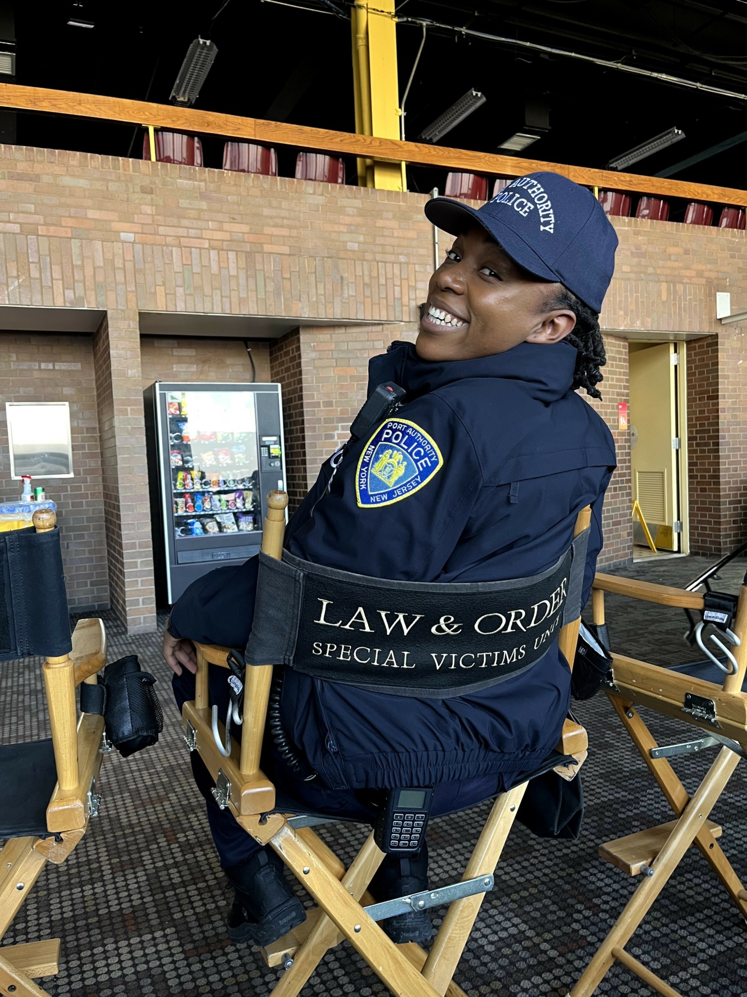 Police officer sitting on a chair, smiling, in an indoor setting with vending machines in the background.