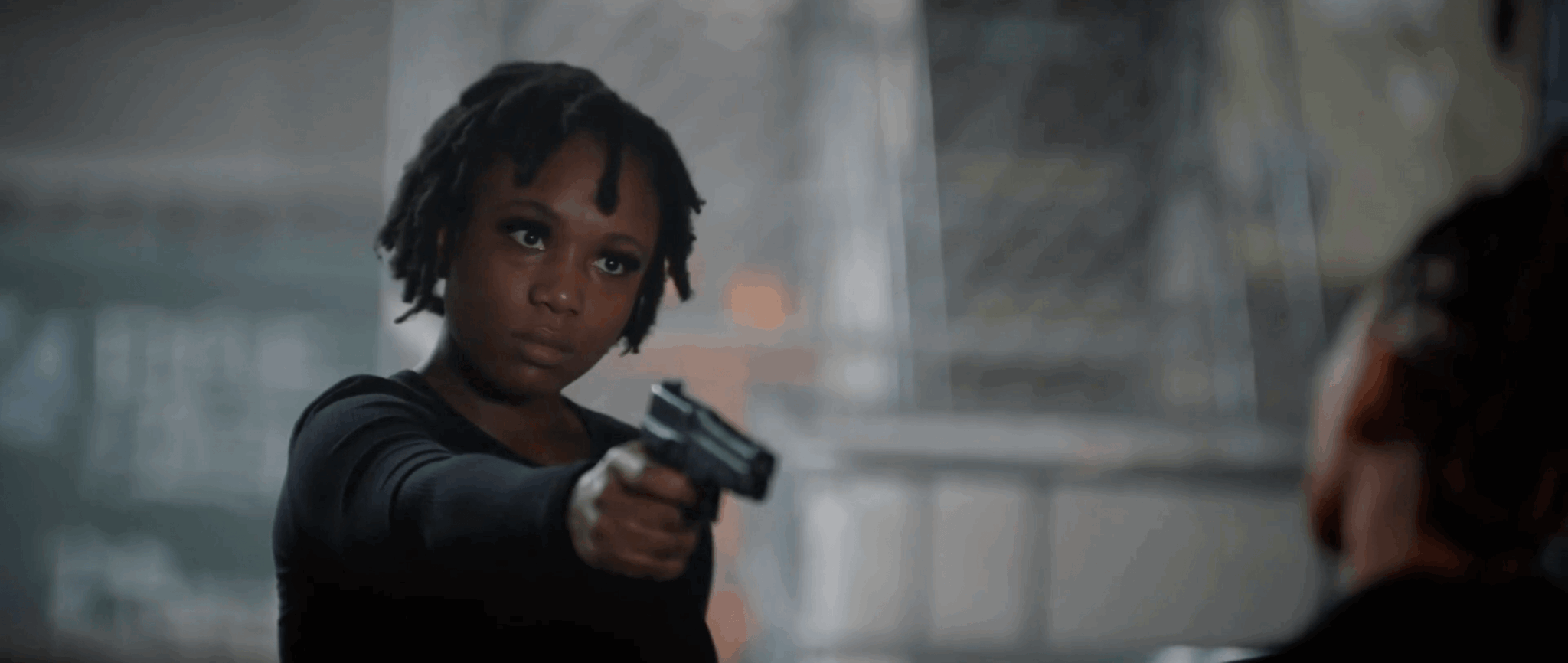Young person with dreadlocks holding a gun, pointing it at another person, in an urban setting.